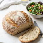 Glutenfreies Sauerteigbrot serviert mit bunter Blattsalat — Eine abgeschnittene, saftige Scheibe des getreidefreien Brotes liegt einladend neben frischem Salat.