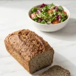 Reissauerteig-Brot serviert mit bunter Blattsalat — Eine umgedrehte, perfekt aufgeschnittene Scheibe des veganen Brotes liegt neben knackigem Salat.