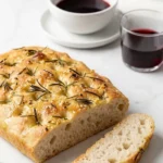 Rosmarin-Knoblauch-Fladenbrot serviert mit italienischer Rotwein — Aufgeschnittenes Hefebrot neben einem Glas Wein.