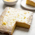 Zitronenkuchen vom Blech serviert mit Filterkaffee — Ein saftiges Kuchenquadrat liegt neben einer Tasse heißem Kaffee.