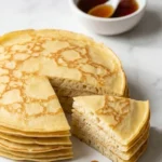 Pfannkuchen, Crêpe und Pancake serviert mit Ahornsirup — Ein aufgeschnittener Pfannkuchenstapel neben einer Schale Sirup.