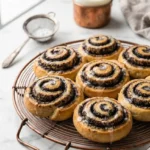 Mohnschnecken serviert mit Milchkaffee — Eine halbierte Hefeschnecke offenbart die vielen saftigen Mohnschichten neben Kaffee.