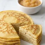 Klassische Eierkuchen serviert mit Apfelmus — Ein zusammengerollter Pfannkuchen aufgeschnitten neben fruchtigem Apfelkompott.
