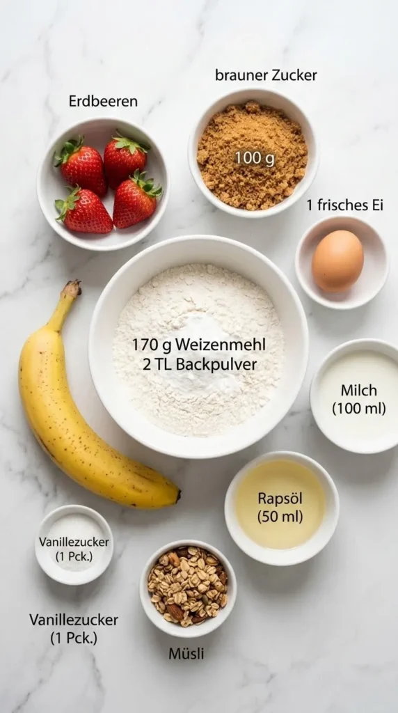 Zutaten für Bananen-Erdbeermuffins: Mehl, brauner Zucker, Ei, Milch, Rapsöl, Banane, Erdbeeren und Müsli auf weißem Marmor.