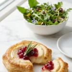 Blätterteig-Häppchen mit Camembert serviert mit Wildkräutersalat — Ein knuspriges Häppchen aufgeschnitten neben frischem Salat.