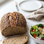 Das schnelle Sauerteigbrot serviert mit bunter Blattsalat — Eine abgeschnittene, saftige Schrotbrotscheibe liegt appetitlich neben frischem Salat.