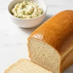 Hausgemachtes Kastenbrot serviert mit Kräuterbutter — Eine aufgeschnittene, ultra-weiche Scheibe zeigt die feine Brotstruktur.