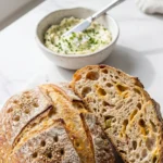 Oliven-Speck-Käse-Brot serviert mit Kräuterbutter — angeschnittener Brotlaib zeigt saftige Krume mit Oliven- und Speckstücken.