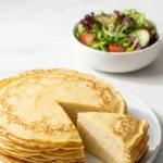 Eierkuchen serviert mit bunter Blattsalat — Ein gefalteter, saftiger Pfannkuchen liegt appetitlich neben einer Schale Salat.
