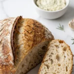 Rosmarin-Knoblauch Artisan Brot serviert mit Kräuterbutter — angeschnittenes Brot zeigt die weiche, offen porige Krume.