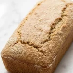 Low Carb Bananenbrot frisch gebacken — Saftiges, zuckerfreies Protein-Bananenbrot in der Kastenform auf weißem Marmor.