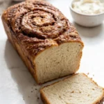 Sauerteig-Rest Zimt Brot serviert mit milder Frischkäse — Eine abgeschnittene, saftige Brotscheibe mit Zimtwirbeln neben Frischkäse.