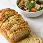 Zupfbrot mit Kräuterbutter serviert mit bunter Blattsalat — Ein abgebrochenes, buttriges Teigstück liegt einladend neben frischem Salat.