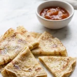 Sauerteig-Crepes serviert mit Marmelade — Ein zarter Pfannkuchen gefaltet neben einer Schale mit fruchtiger Konfitüre.