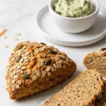 Karotten-Brötchen serviert mit Kräuterbutter — aufgeschnittenes Brötchen zeigt die saftige Krume mit Kernen.