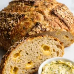 Schnelles Airfryer-Brot serviert mit Kräuterbutter — Eine abgeschnittene Brotscheibe zeigt geschmolzene Cheddar-Taschen.