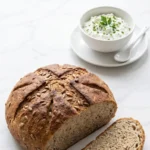 Low-Carb-Brot aus dem Airfryer serviert mit frischer Kräuterquark — Eine abgeschnittene, saftige Scheibe Saatenbrot liegt einladend neben Quark.