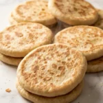 Indisches Naanbrot frisch gebacken — krosse, runde Brotfladen mit typischen Röstflecken auf weißem Marmor.