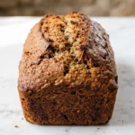 Einfaches Bananenbrot frisch gebacken — saftiges, dunkel-goldbraunes Kastenbrot mit feiner Kruste auf weißem Marmor.