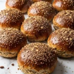 Burger-Buns frisch gebacken — extra softe, glänzende Hamburger-Brötchen überstreut mit viel Sesam auf weißem Marmor.