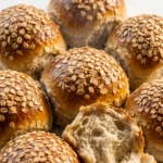 Haferflocken-Brötchen frisch gebacken — extra softe, glänzende Frühstücksbrötchen überstreut mit viel Haferflocken auf weißem Marmor.