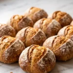 Frühstücksbrötchen über Nacht frisch gebacken — krosse goldbraune Kruste mit ausgeprägtem Kreuzschnitt auf weißem Marmor.