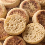Englische Toasties frisch gebacken — krosse, runde Toastbrötchen mit grießbemehlter Kruste auf weißem Marmor.