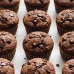 Saftige vegane Schoko Bananen Muffins mit Sauerteig frisch gebacken — dunkelbraun mit Schokostückchen.