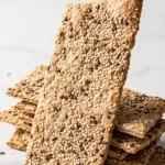 Sauerteig Cracker frisch gebacken — knuspriges Knäckebrot mit reichlich Sesam auf einer rustikalen Holzoberfläche