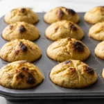 Sauerteig-Focaccia-Muffins frisch gebacken — 12 portionierte Mini-Focaccias mit Rosmarin in einer dunklen Muffinform auf Marmor