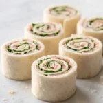 Wrap-Röllchen frisch gebacken — farbenfrohe Fingerfood-Häppchen mit Putenbrust und Gurkenspirale auf weißem Marmor.