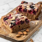 Beerenkuchen aus Vollkorn und Sauerteigresten frisch gebacken — saftige Kuchenstücke mit Beeren und Mandelstiften auf Holzbrett