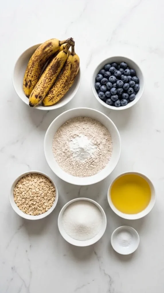 Zutaten für veganen Bananen-Heidelbeer-Kuchen: Vollkornmehl, reife Bananen, Heidelbeeren, Haferflocken, Pflanzenöl, Zucker und Salz.