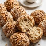 Körnerbrötchen nach Paniniart frisch gebacken — knusprige Mehrkornbrötchen mit reichem Saatenbelag auf weißem Marmor.