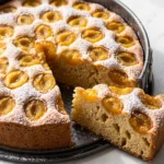 Klassischer Mirabellenkuchen frisch aus der Springform mit Puderzucker bestäubt und zwei angeschnittenen Stücken.