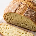 Saftiges Zucchini-Kartoffel-Brot im Topf gebacken — knuspriges Topfbrot angeschnitten auf Holzbrett.