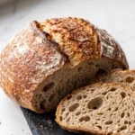Sauerteigbrot aus der Heißluftfritteuse auf Schieferbrett mit tiefer Bäckermaserung und zwei dicken Scheiben.