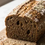Vollkorn-Zucchini-Kastenbrot frisch gebacken und angeschnitten auf Holzbrett mit Hanfsamen-Topping.