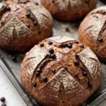 Aronia-Sauerteigbrot frisch gebacken — dunkle Kruste mit Einschneidung und Bemehlung