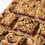 Saftiger Zwetschgen-Streuselkuchen mit Sauerteig und Haselnüssen frisch vom Blech, in Stücke geschnitten.
