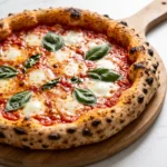 Neapolitanische Sauerteig-Pizza frisch aus dem Ofen auf Holzschieber mit Leopard-Muster am Rand, Mozzarella und Basilikum.