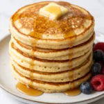 Fluffige Sauerteig Pancakes als hoher Stapel mit schmelzender Butter, Ahornsirup und frischen Beeren serviert.