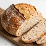 Klassisches Dinkel-Sauerteigbrot ohne Hefe frisch gebacken aus dem Gusseisentopf, angeschnitten auf Holzbrett.