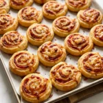 Herzhafte Blätterteigschnecken mit Tomate und Käse frisch gebacken und knusprig auf einem Holzbrett serviert.