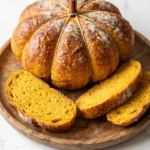 Saftiges Sauerteig-Kürbisbrot in Kürbisform frisch gebacken, angeschnitten auf einem Holzbrett mit leuchtend oranger Krume.
