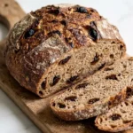 Saftiges Walnuss-Pflaumenbrot mit Sauerteig frisch aus dem Dutch Oven, knusprig gebacken und angeschnitten auf Holzbrett.