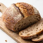 Sauerteig-Bauernbrot ohne Hefe frisch gebacken aus dem Dutch Oven, knusprig aufgerissen und angeschnitten auf einem Holzbrett.