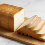 Fluffiges Sauerteig-Toastbrot frisch gebacken aus der Kastenform, gleichmäßig in Scheiben aufgeschnitten auf Holzbrett.