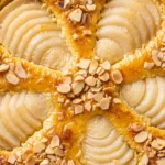 Feiner Birnenkuchen mit Guss und gerösteten Mandeln frisch gebacken, angeschnitten auf einer Tortenplatte.