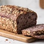 Saftiges Aronia-Dinkelbrot mit Haferflockenkruste und Kernen frisch aus der Kastenform gebacken, angeschnitten auf Holzbrett.